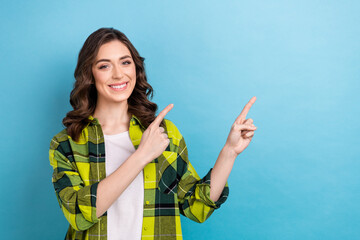 Sticker - Portrait of cheerful pretty girl wavy hairstyle wear plaid jacket indicating at discount empty space isolated on blue color background