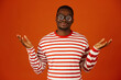 African young man standing over orange background with clueless and confused expression and hands raised