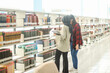 © Queenmoonlite Studio - Young Muslim female student with her Asian friend choosing books to read at library for studying, academic research, or school work or project