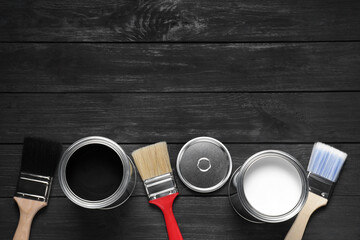 Cans of white and black paints with brushes on wooden table, flat lay. Space for text