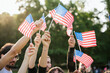 Group of people holds flags of the United States of America USA in the air celebrating citizenship at sunset outdoor - Copy space