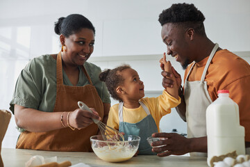 Wall Mural - Happy African American family in aprons baking together with little girl in the kitchen at home