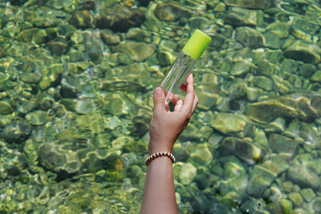 Girl's hand holding cosmetic transparent bottle with body eco spray in front of the sea. fresh marine scented cosmetics mock up