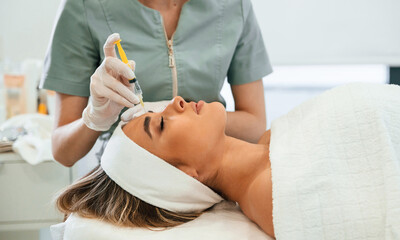 Wall Mural - View from the side. Making injection. Woman face getting facial care by beautician hands at spa salon