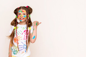 Wall Mural - A little schoolgirl with painted hands and face with multicolored paints. A girl stained with paints. The concept of children's creativity. Funny child draws with his hands. Copy space. Banner.