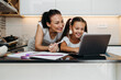 © Dusko - Young mother helping her daughter on e-learning session during virus pandemic crisis lockdown or quarantine. Illness prevention and new normal concept.
