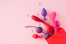 Erotic Toys For Adults Concept. Top View Arrangement Of Shopping Bag, Vibrator, Anal Plugs, Vaginal Balls, Colorful Hearts On Pastel Pink Background With Empty Space For Text Or Promotional