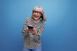 well-groomed slender 60s middle-aged woman holding a smartphone with a mockup on a bright background with copy space