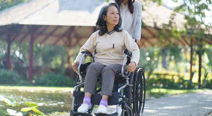 Asian senior woman in wheelchair with happy daughter. Family relationship retired woman sitting on wheelchair in the park age care at retirement home.