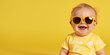 Funny baby wearing big sunglasses. Isolated on bright yellow background. Summer banner, copy space.