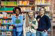 © pikselstock - Group of diverse students smiling at camera while standing together in a library