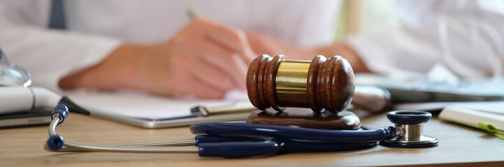 Court gavel with stethoscope on a table in background doctor writes notes