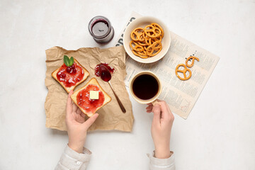 Wall Mural - Woman eating tasty toasts with cranberry jam and drinking coffee on light background