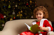 © oksix - Beautiful little girl sits on the chair next to a nicely decorated Christmas tree