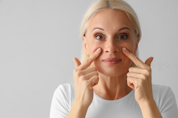 Poster - Mature woman doing face building exercise on light background, closeup