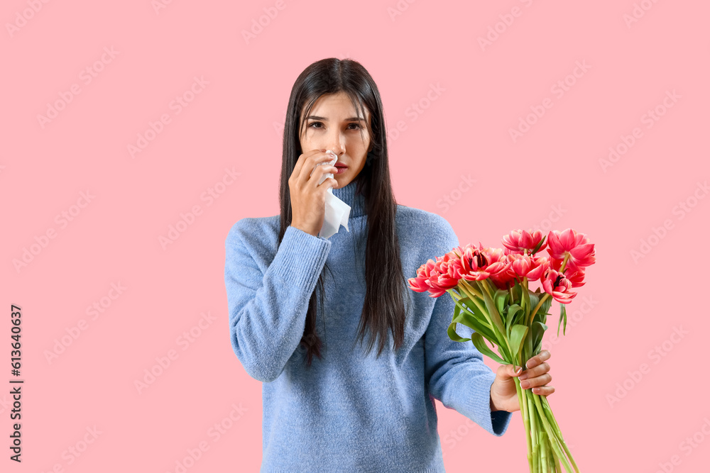 Allergic young woman with tulips sneezing on pink background