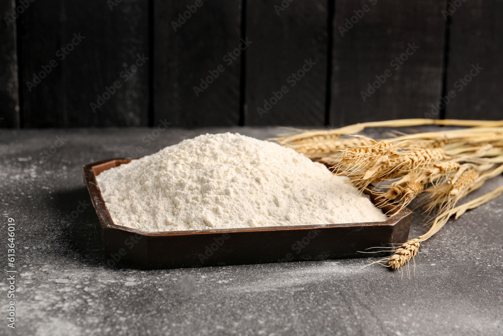 Plate with flour and wheat ears on grunge black background