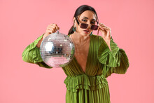 Fashionable Beautiful Woman In Green Dress And Sunglasses With Disco Ball Posing On Pink Background