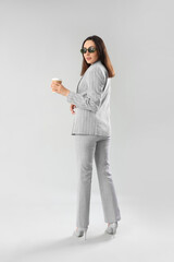Wall Mural - Young woman in stylish suit with cup of coffee on light background