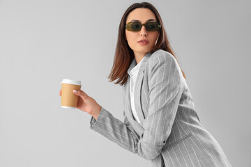 Wall Mural - Young woman in stylish suit with cup of coffee on light background