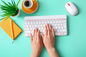 Female programmer using computer keyboard with cup of coffee, mouse and notebook on turquoise background