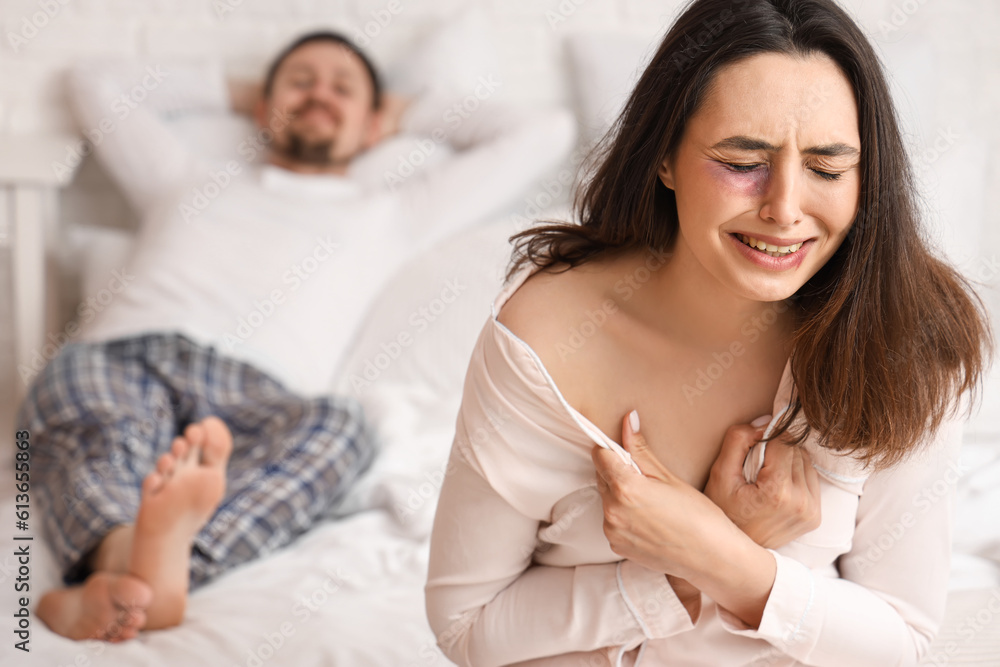 Crying young woman with bruises in bedroom. Domestic violence concept