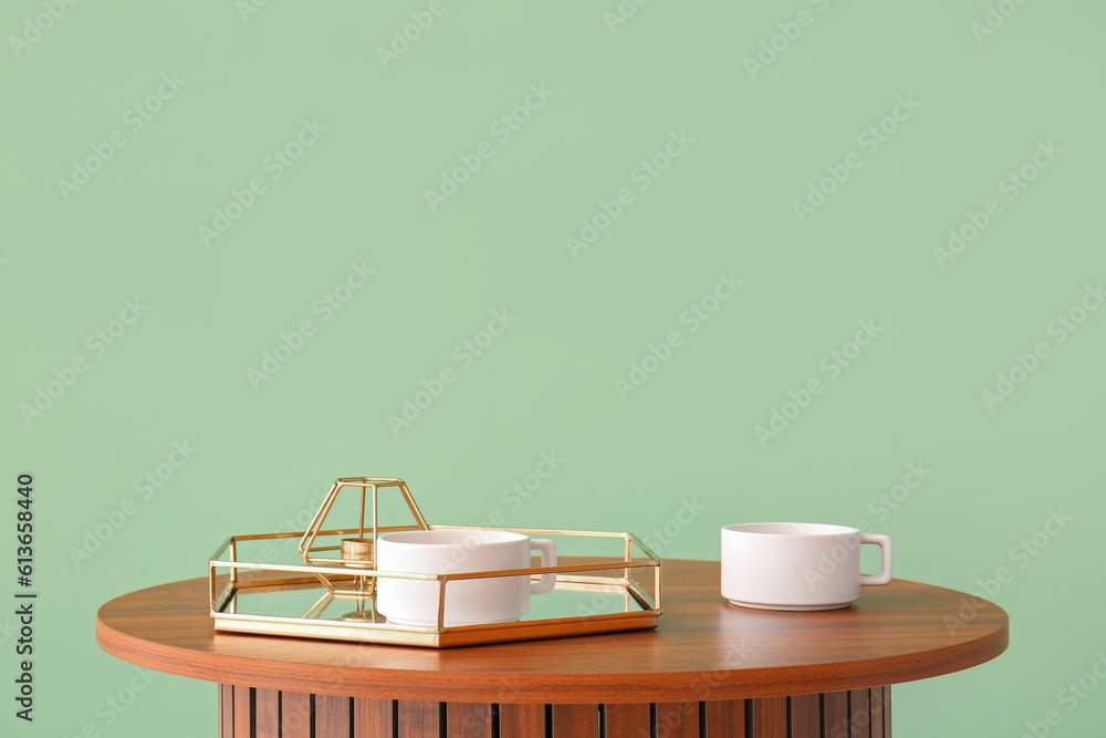 Wooden coffee table with tray and cups near green wall