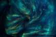 Abstract magic blue background with golden sparkles. Photo of a blue liquid with gold glitters and green tints. Various shades of green and blue with golden splashes and flows. 
