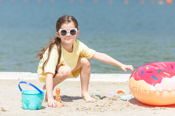 Wall Mural - Little girl playing on the beach on summer holidays. Child having fun with a sand on the city lake seashore. Vacation concept. Happy sunny day