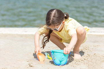 Wall Mural - Little girl playing on the beach on summer holidays. Child having fun with a sand on the city lake seashore. Vacation concept. Happy sunny day