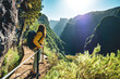 © Michael - Backpacker woman enjoying scenic view from below large rock wall along water channel at steep cliff through Madeira's rainforest. Levada of Caldeirão Verde, Madeira Island, Portugal, Europe.
