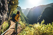 © Michael - Backpacker woman enjoying scenic view from below large rock wall along water channel at steep cliff through Madeira's rainforest. Levada of Caldeirão Verde, Madeira Island, Portugal, Europe.