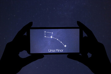 Woman using stargazing app on her phone at night, closeup. Identified stick figure pattern of Little Bear (Ursa Minor) constellation on device screen
