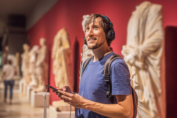 Portrait of contemporary man looking at sculptures and listening to audio guide at museum exhibition