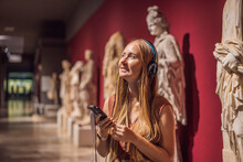 Portrait Of Contemporary Young Woman Looking At Sculptures And Listening To Audio Guide At Museum Exhibition