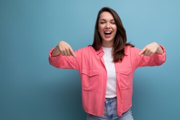 Sticker - cheerful brunette lady in a pink shirt and jeans points her finger at the infomation on a studio background