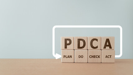 PDCA text ,means Plan Do Check Act, on wooden cube block with loop line including copy space. For business strategy goal success concept