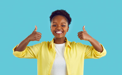 I like that. Joyful dark-skinned woman making thumb up sign showing her support and respect to you. Close up of smiling African American young woman giving two thumbs up on light blue background.