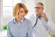 © Studio Romantic - Mature smiling female patient in the clinic for a medical checkup. Senior physician doctor with stethoscope examining woman's lungs, breathing and heartbeat at the hospital in exam room.