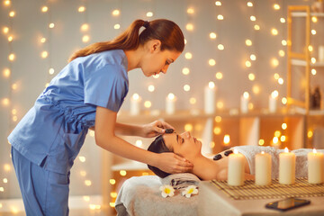 Wall Mural - Beautiful young woman enjoying massage in spa salon. Side view portrait of beautician making face massage to relaxed female client. Facial beauty treatment, body care, wellness