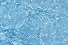 Blue Water With Ripples On The Surface. Defocus Blurred Transparent Blue Colored Clear Calm Water Surface Texture With Splashes And Bubbles. Water Waves With Shining Pattern Texture Background.