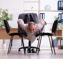 Wall Mural - Old male employee doing physical exercises at workplace