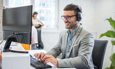 Wall Mural - Middle aged businessman using a headset and computer in a modern office.