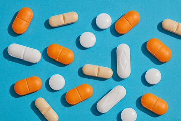 Many medical pills of different colors and shapes scattered decorated on a blue background. Pharmaceutical pills and vitamins. Health budget concept.