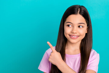 Wall Mural - Photo of dreamy sweet little child dressed pink t-shirt showing finger looking empty space isolated teal color background