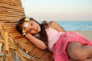  beauteful balkan little girls with pink dres on the Beach with Long Hair and wreath on her head 
lies in a chair  at the sunset 