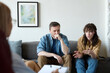 © Mediaphotos - Young woman talking about her family problems to psychologist while they sitting on sofa together with her husband