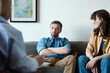 © Mediaphotos - Young couple having argument sitting on sofa and talking to psychologist about their problems