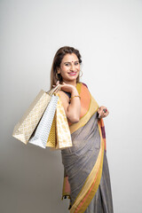 Young Indian woman wearing saree outfit and holding shopping bags on white background.