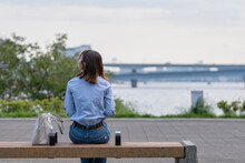 海の近くの公園のベンチに座る女性の後ろ姿